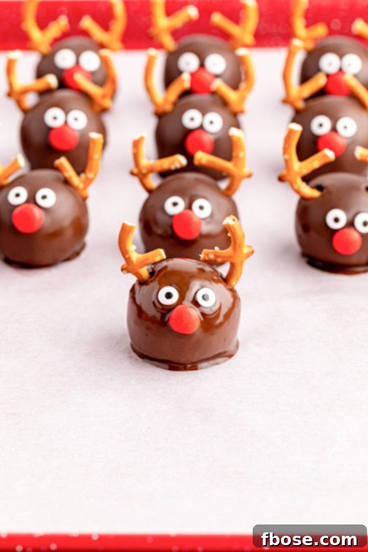 Reindeer Oreo Balls with eyes and noses being added on a parchment-lined baking sheet during assembly.