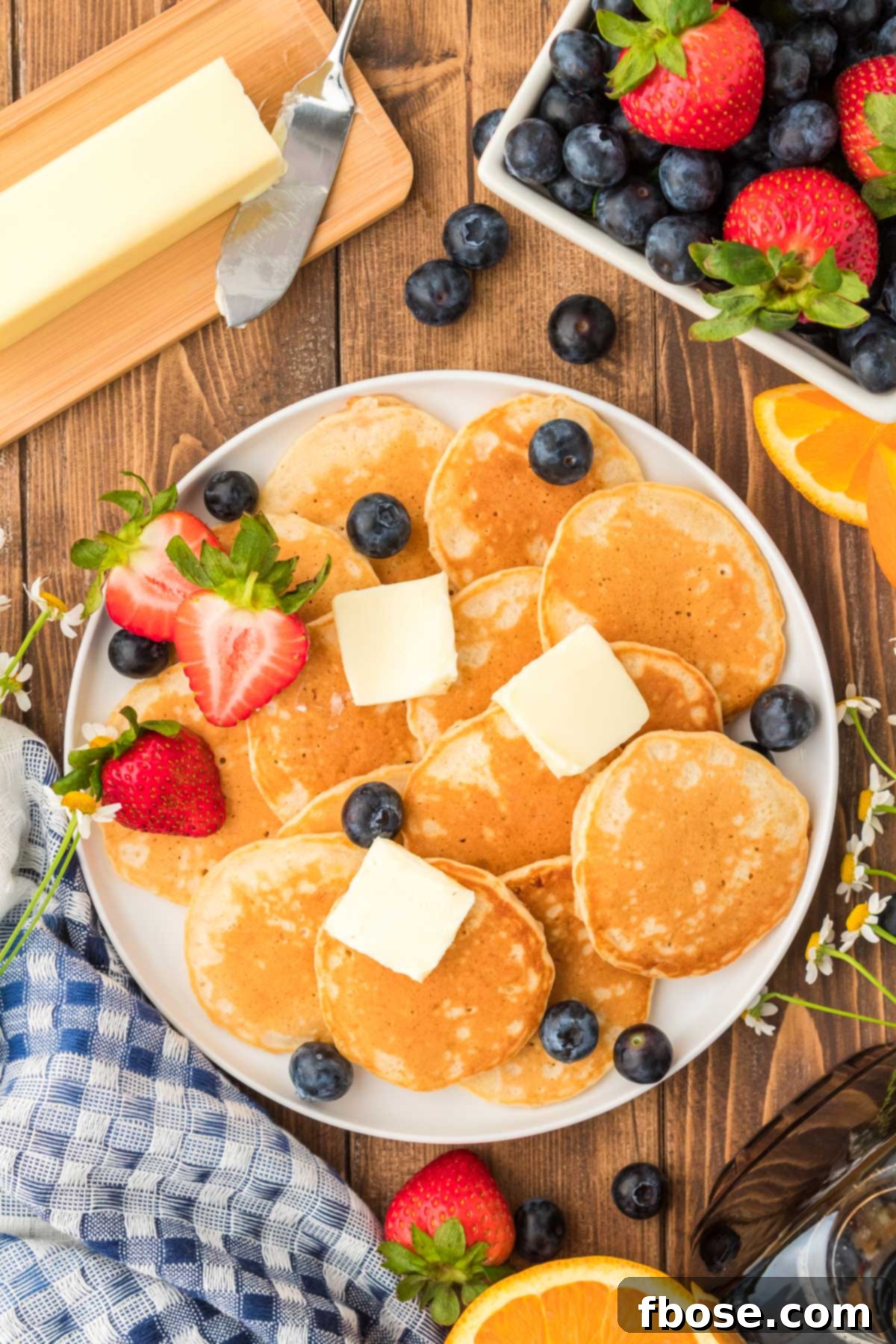 Fluffy Coin Pancakes 3 Overhead photo of a plate of silver dollar pancakes beautifully arranged with fresh butter and a scattering of vibrant berries.