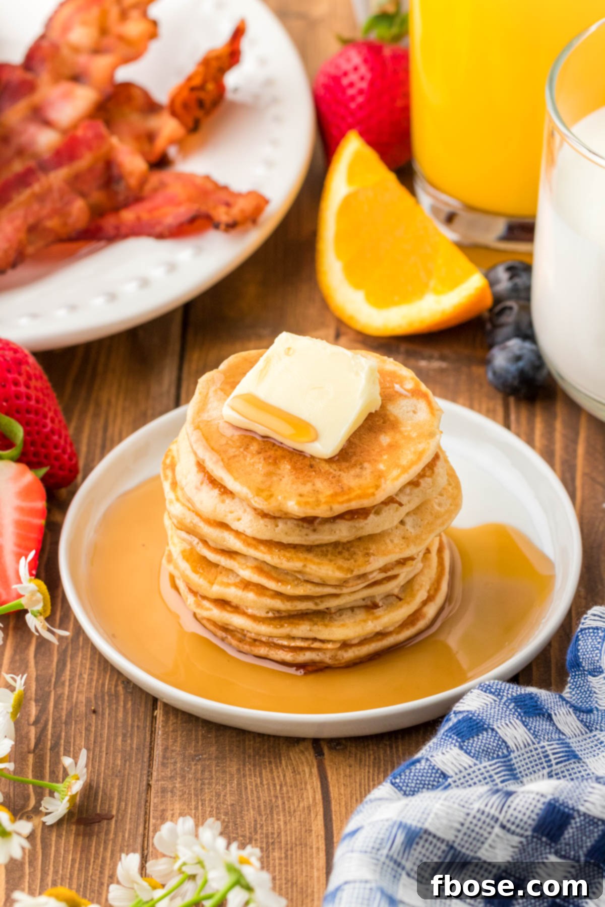 Fluffy Coin Pancakes 7 A stack of perfectly golden silver dollar pancakes on a white plate, resting on a rustic wooden table, ready to be enjoyed.
