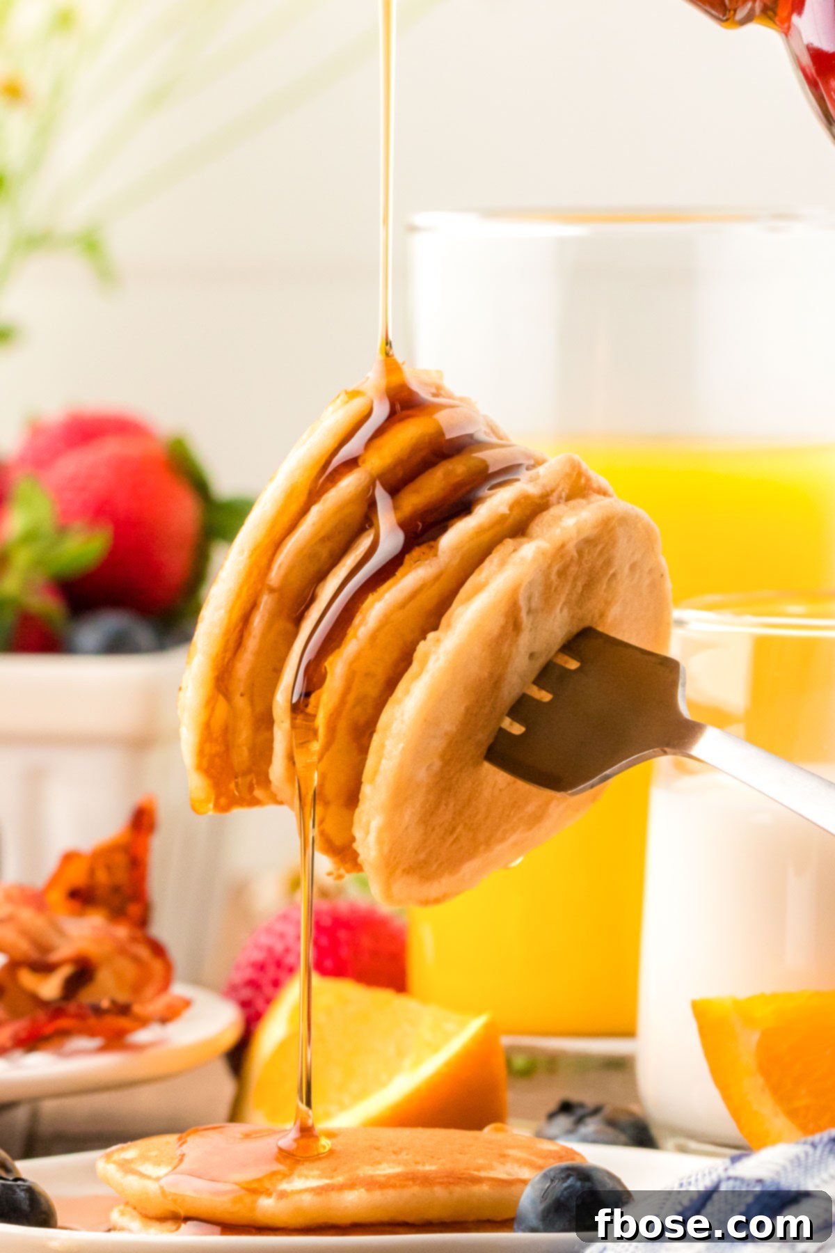 Fluffy Coin Pancakes 9 Golden syrup cascading over a stack of fluffy pancakes, held aloft by a fork, promising a delightful bite.