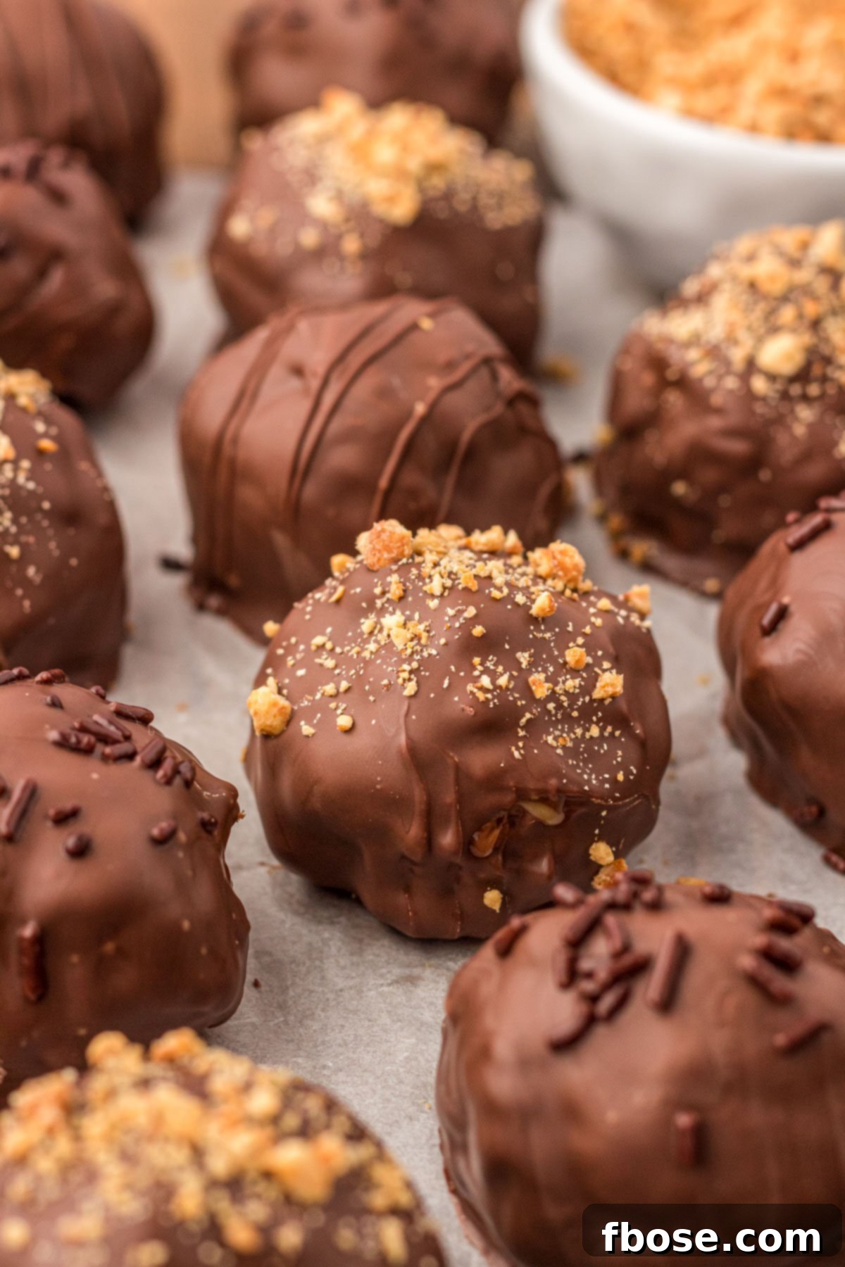 No-Bake Peanut Butter Crunch Bites 11 A generous display of Rice Krispie Peanut Butter Balls, carefully arranged on a piece of parchment paper, highlighting their crispy, chocolate-coated perfection.