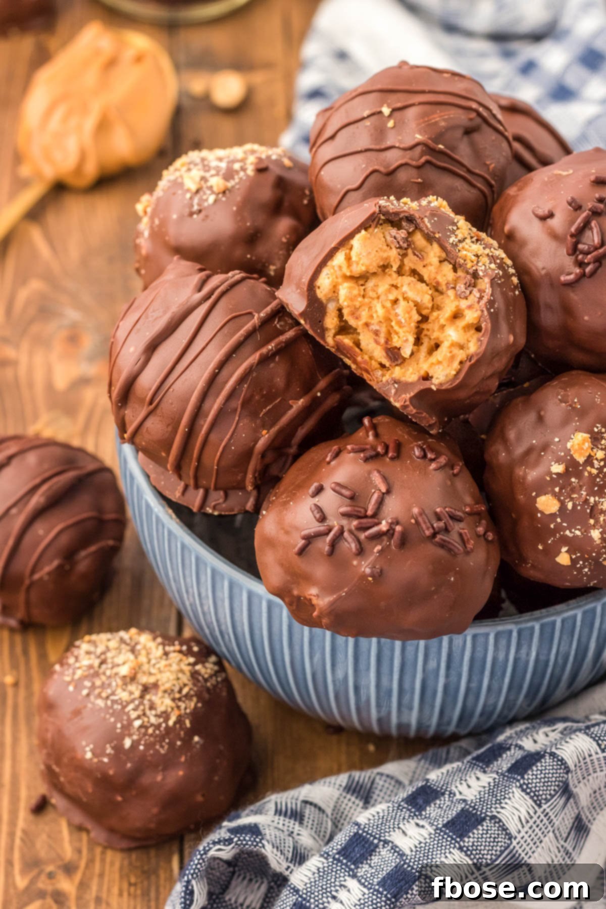 No-Bake Peanut Butter Crunch Bites 12 A blue bowl brimming with chocolate-coated Peanut Butter Balls, one with a bite taken out, showcasing the crispy interior.