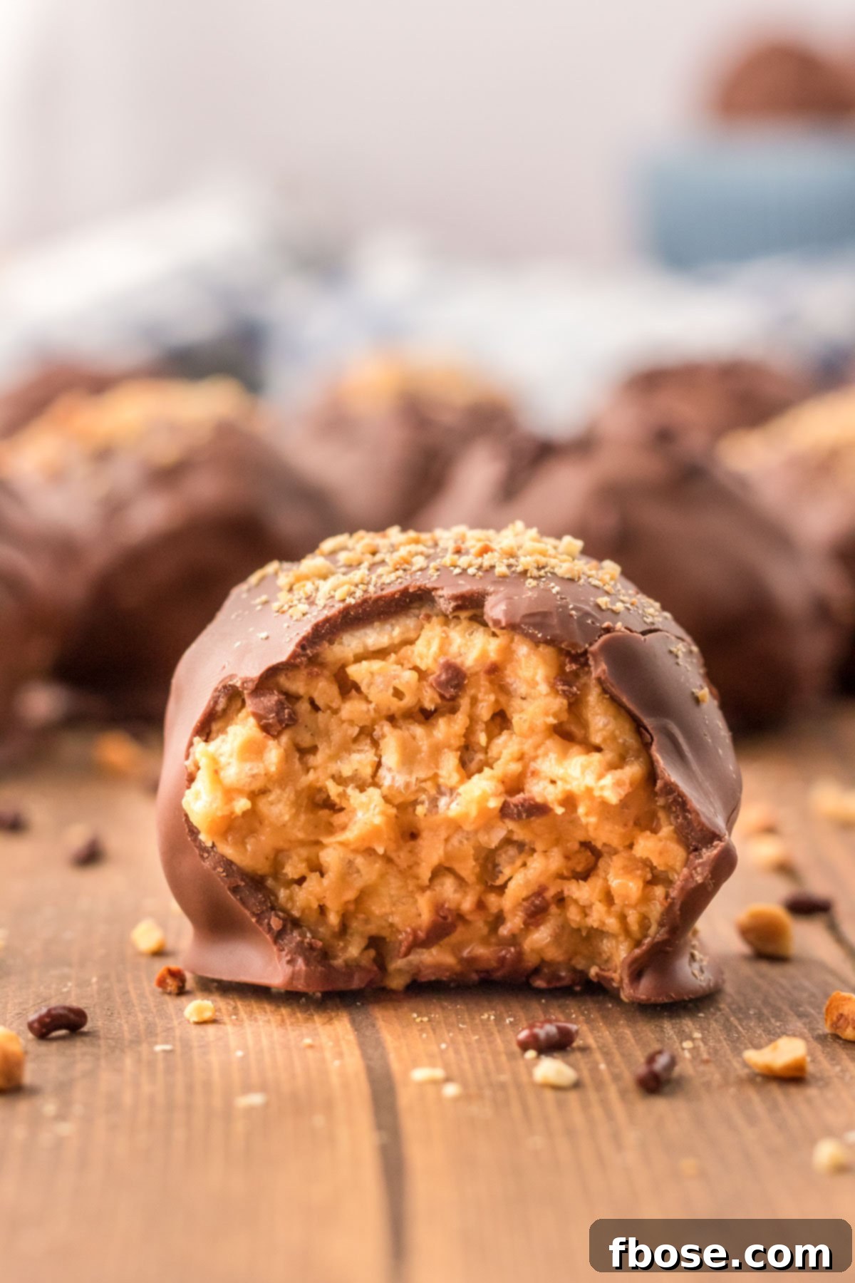 No-Bake Peanut Butter Crunch Bites 3 A single, perfectly formed peanut butter ball rests on a wooden table, with a small bite taken out to reveal its crispy, creamy interior.