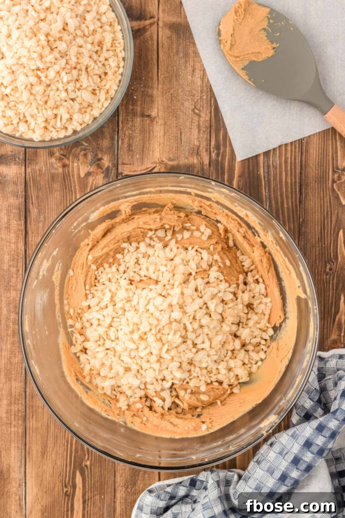 No-Bake Peanut Butter Crunch Bites 7 Crispy Rice Krispies cereal is gently folded into the smooth peanut butter ball mixture in a glass bowl, adding the signature crunch to the treats.
