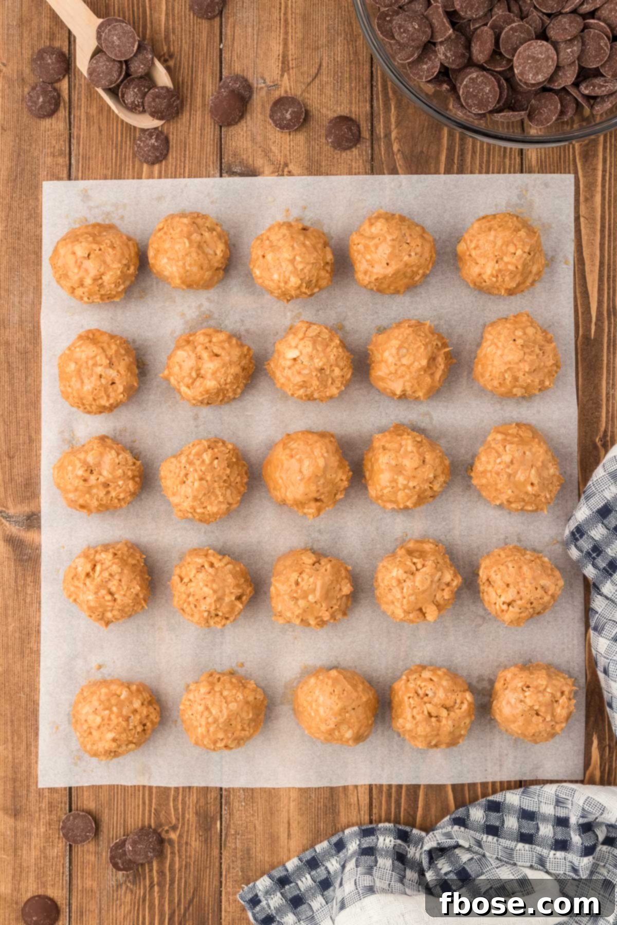 No-Bake Peanut Butter Crunch Bites 8 Perfectly rolled peanut butter balls, uniform in size, are arranged neatly on a parchment-lined baking sheet, ready for their chocolate coating.
