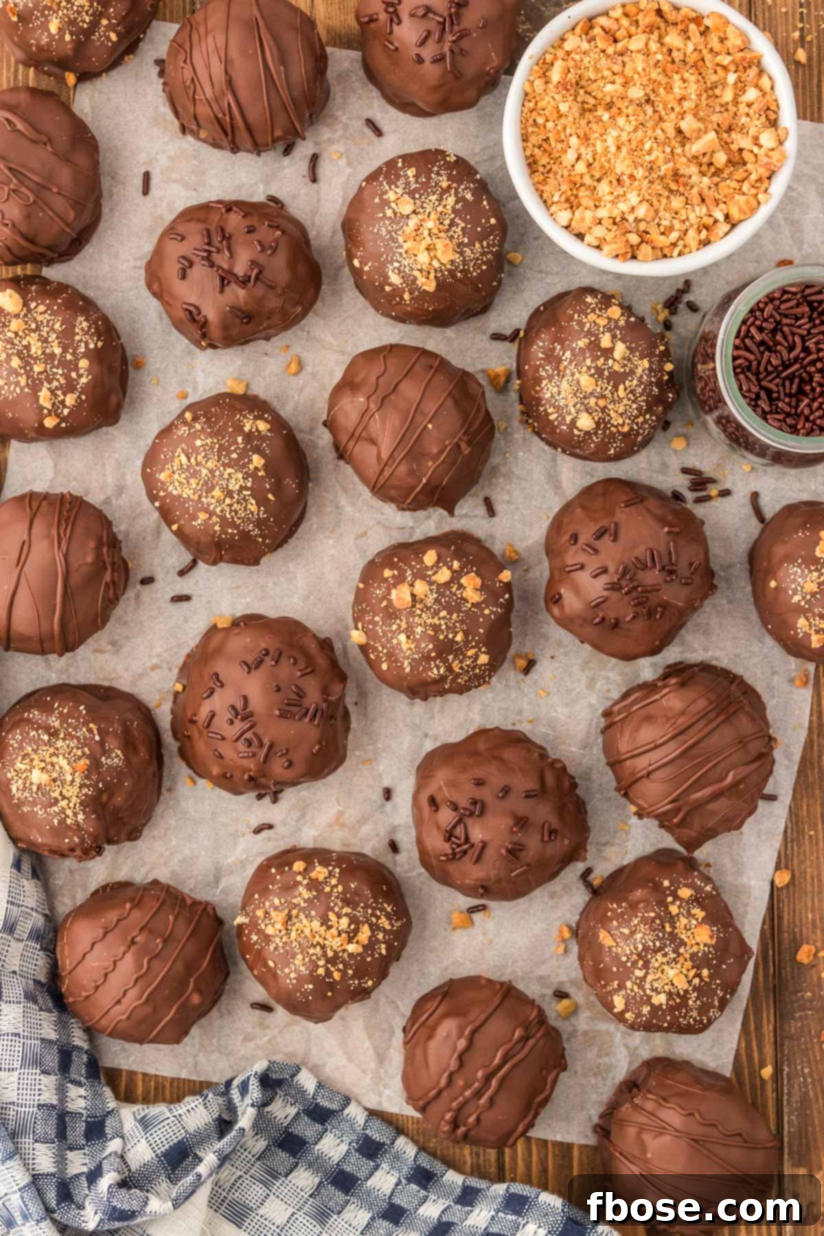 No-Bake Peanut Butter Crunch Bites 10 A freshly dipped Rice Krispie Peanut Butter Ball sits on parchment paper, its smooth chocolate coating beginning to set, alongside other finished treats.
