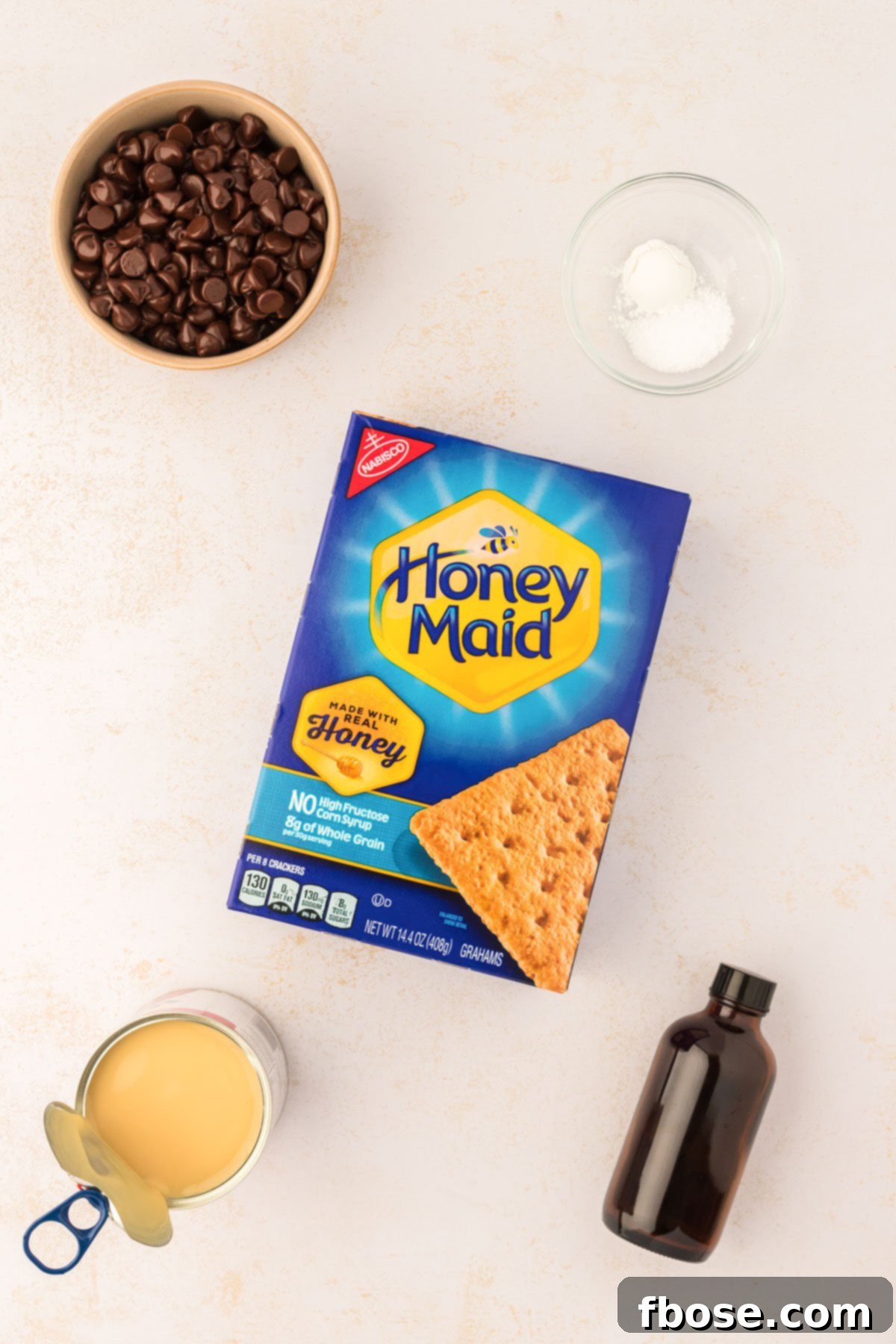 Various ingredients for making graham cracker bars, including whole graham crackers, chocolate chips, and condensed milk, neatly arranged on a kitchen table.