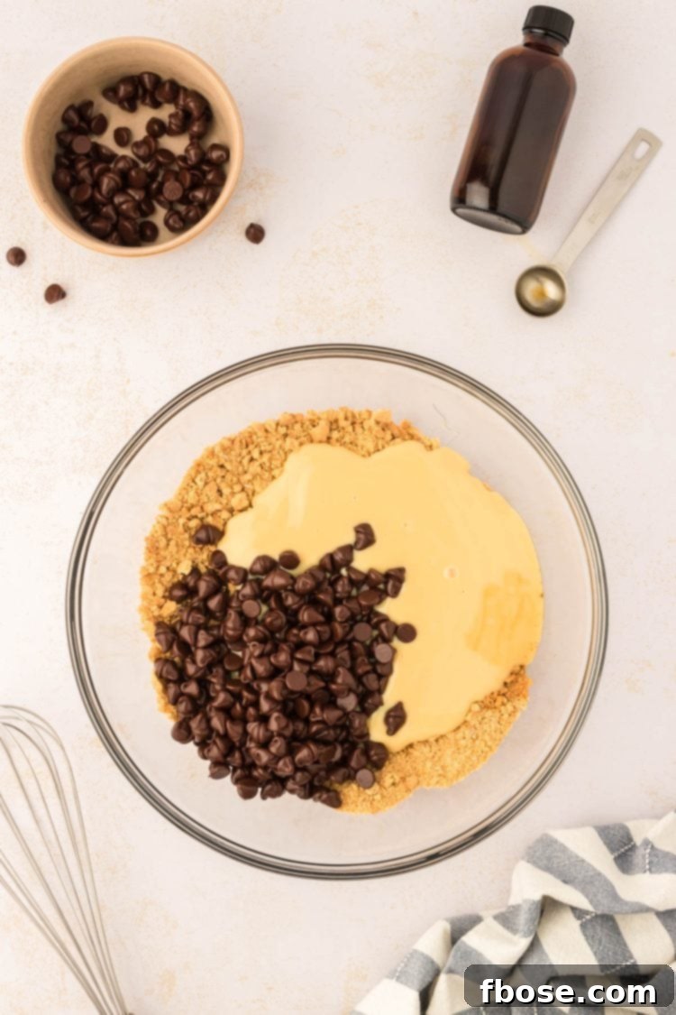 Sweetened condensed milk and chocolate chips being poured into a bowl of graham cracker crumbs, illustrating the combining process.