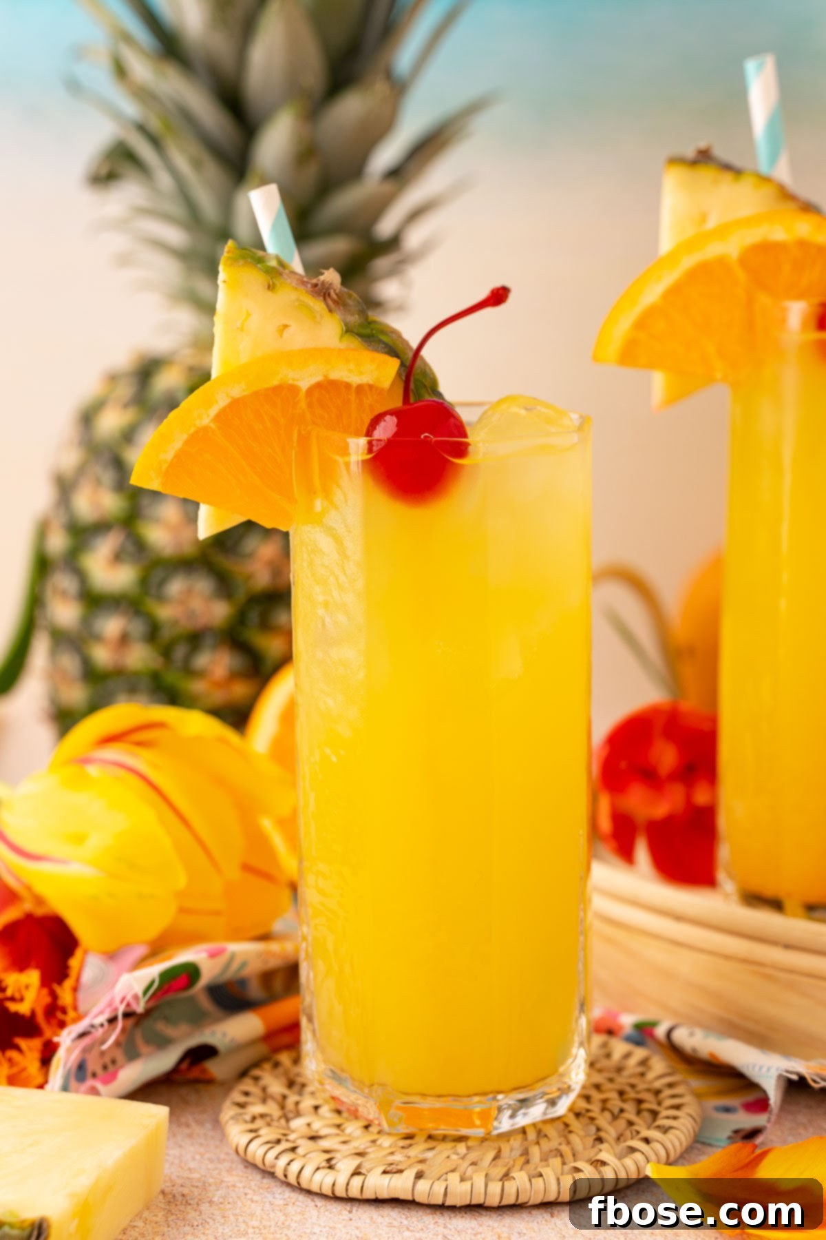 A tall glass of pineapple punch garnished with a cherry, orange slice, and pineapple wedge, set against a bright, inviting backdrop.
