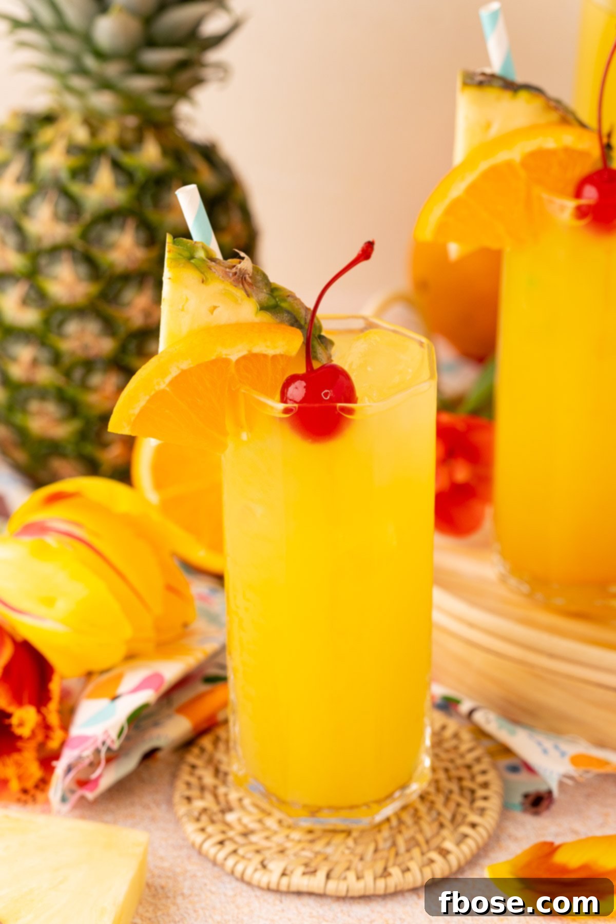 A glass filled with pineapple punch, elegantly surrounded by tropical flowers and fresh pineapple, highlighting its refreshing appeal.