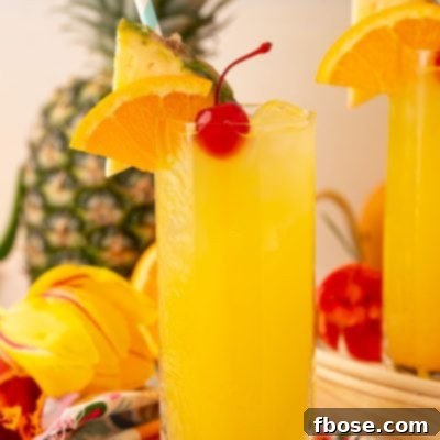 A tall glass of pineapple punch garnished with a cherry, orange slice, and pineapple wedge.