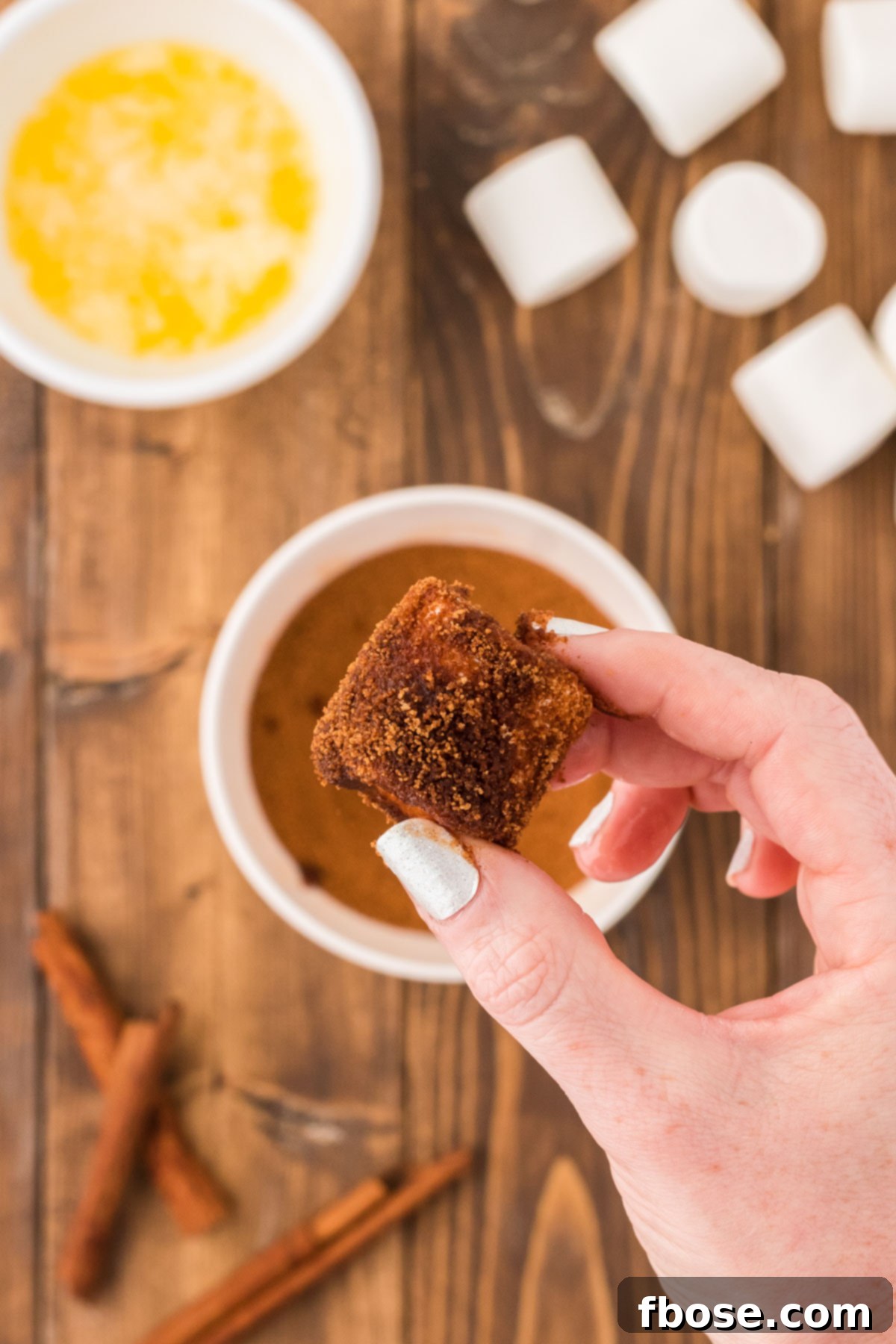 A woman's hand holding a marshmallow that has been coated in brown sugar and cinnamon.