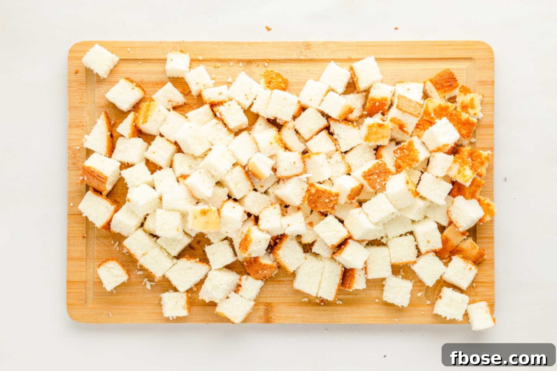 Overhead photo of angel food cake expertly cut into even cubes on a clean cutting board, ready for layering.