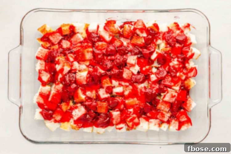 Strawberry pie filling being spread meticulously over the first layer of angel food cake in a pan.