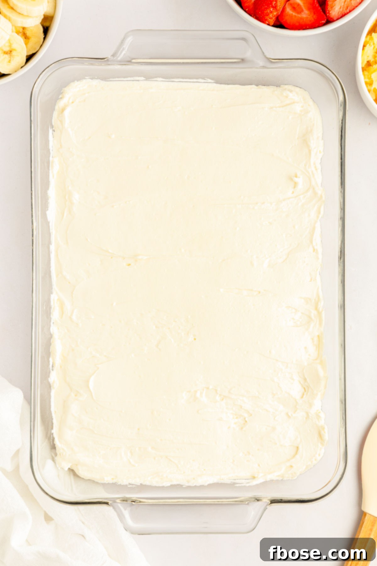 A thick, smooth layer of creamy cheesecake filling spread over the graham cracker crust in a glass baking dish.
