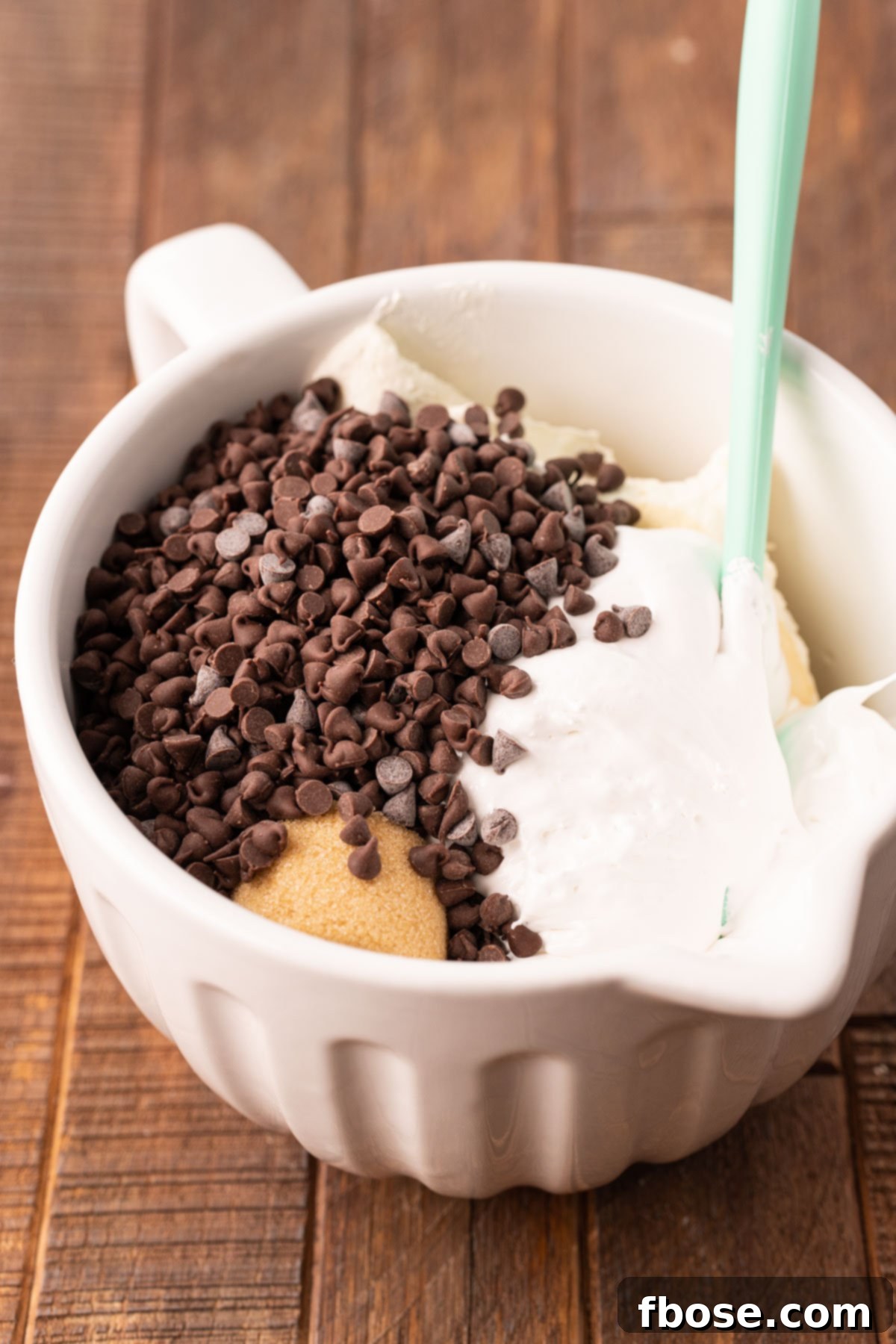 A white mixing bowl filled with the base ingredients for Booty Dip, featuring softened cream cheese and marshmallow fluff, ready to be combined with a blue rubber spatula for a smooth blend.