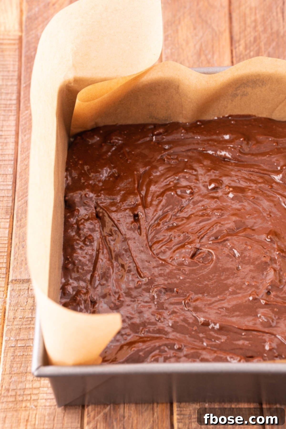 Smooth, rich brownie batter evenly spread in a baking pan lined with parchment paper, perfectly prepared for baking.