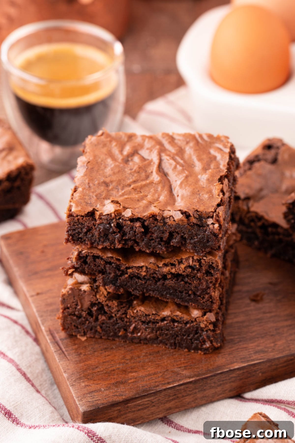A stack of three perfectly baked, fudgy brownies on a wooden board, highlighting their rich color and inviting texture.