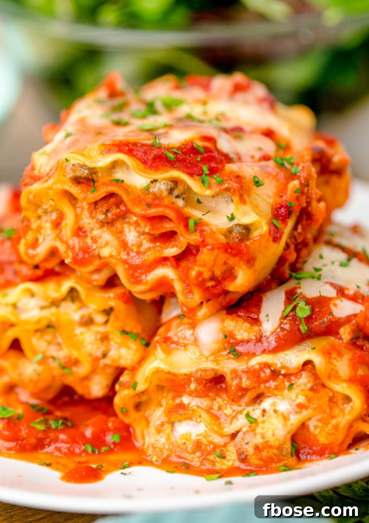 Three golden-brown lasagna roll-ups artfully arranged on a pristine white plate, garnished with fresh basil.