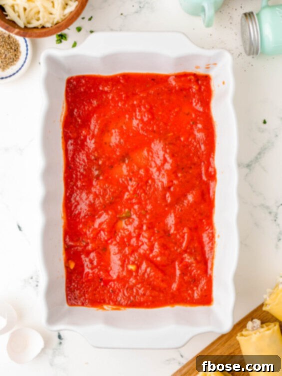 A vibrant red marinara sauce evenly spread across the bottom of a clear baking dish.