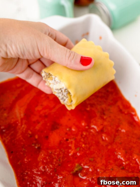 A single lasagna roll-up being carefully placed seam-side down into a baking pan filled with sauce.