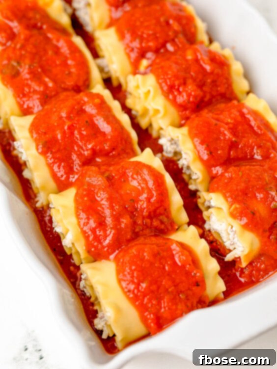 Marinara sauce being poured over neatly arranged lasagna roll-ups in a baking dish, preparing them for the oven.