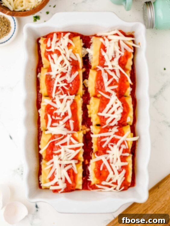 Lasagna roll-ups nestled in a baking dish, generously topped with mozzarella cheese and marinara sauce, ready to be baked.