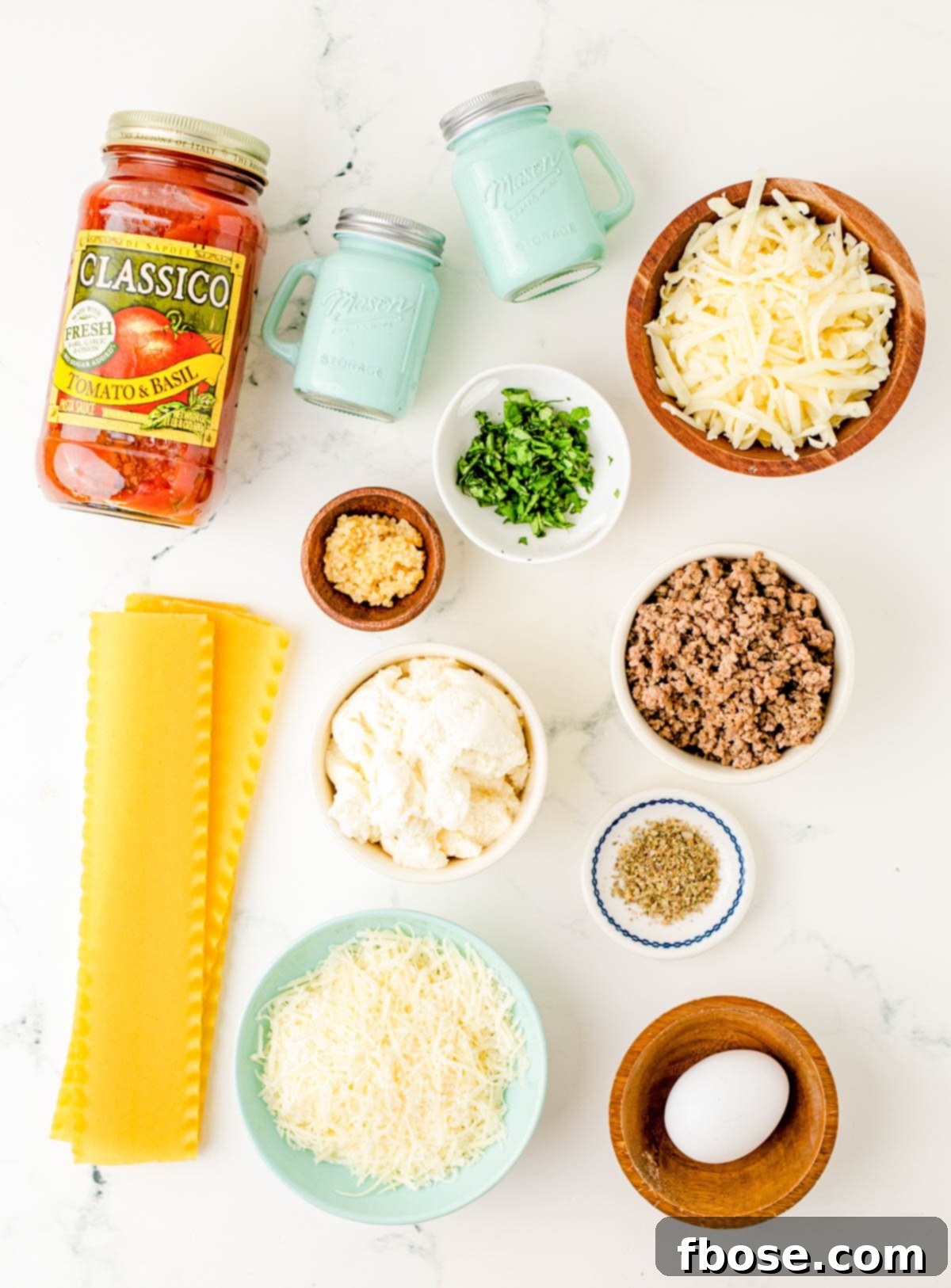 An inviting overhead photo of all the fresh ingredients meticulously laid out to prepare lasagna roll-ups, featuring cheeses, herbs, pasta, and sauce.