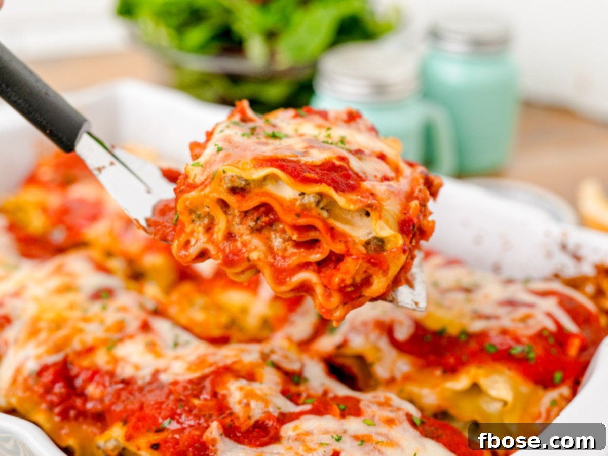 A close-up of a spatula gently scooping a perfectly baked, cheesy lasagna roll-up from a pan, highlighting its golden crust and creamy interior.