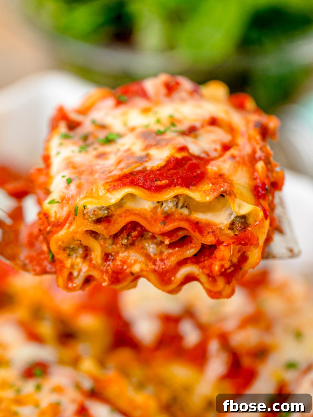 A close-up of a golden-brown lasagna roll-up being lifted from the baking pan with a spatula, showcasing its perfectly cooked state.