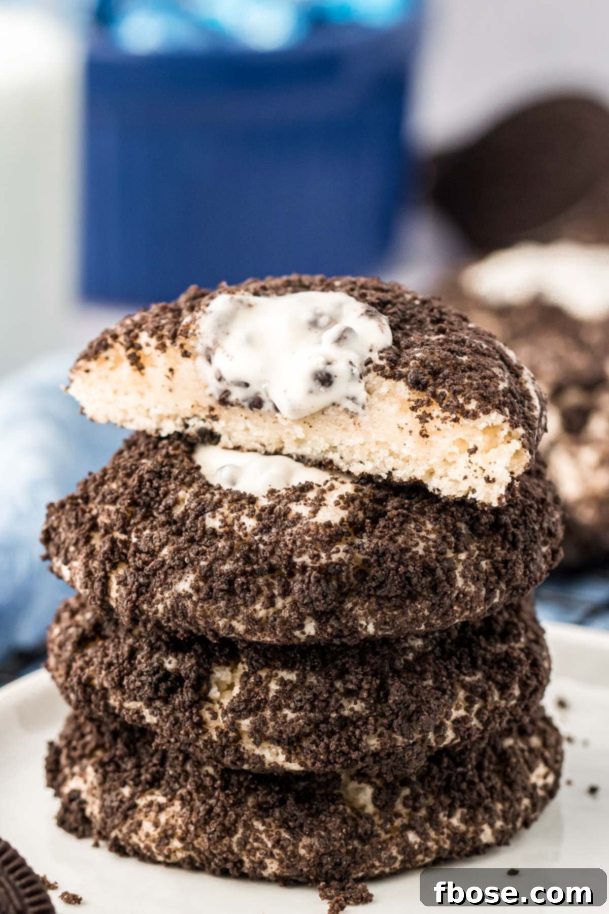 A stack of four Oreo thumbprint cookies on a white plate, the top one has been cut in half, revealing the soft center.