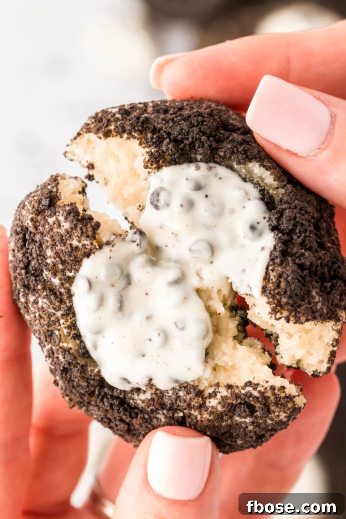 A woman's hand breaking an Oreo thumbprint cookie in half, revealing its soft, creamy center and crunchy exterior.