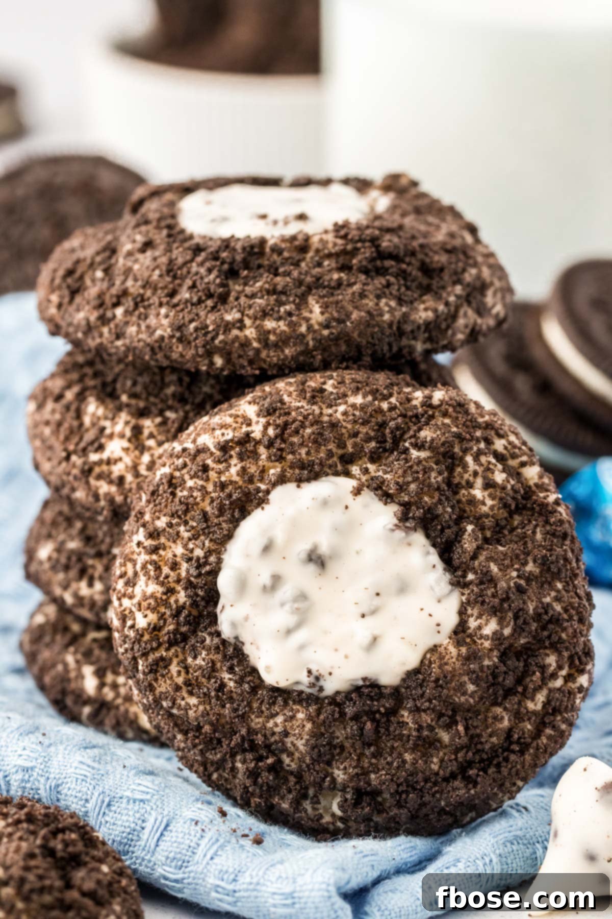 A stack of Oreo thumbprint cookies with one leaning against it, showcasing the inviting cookies and cream topping.