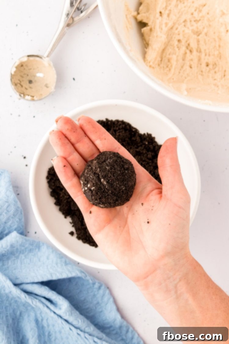 An Oreo-coated cookie dough ball held gently in a woman's hand, perfectly prepared for baking.