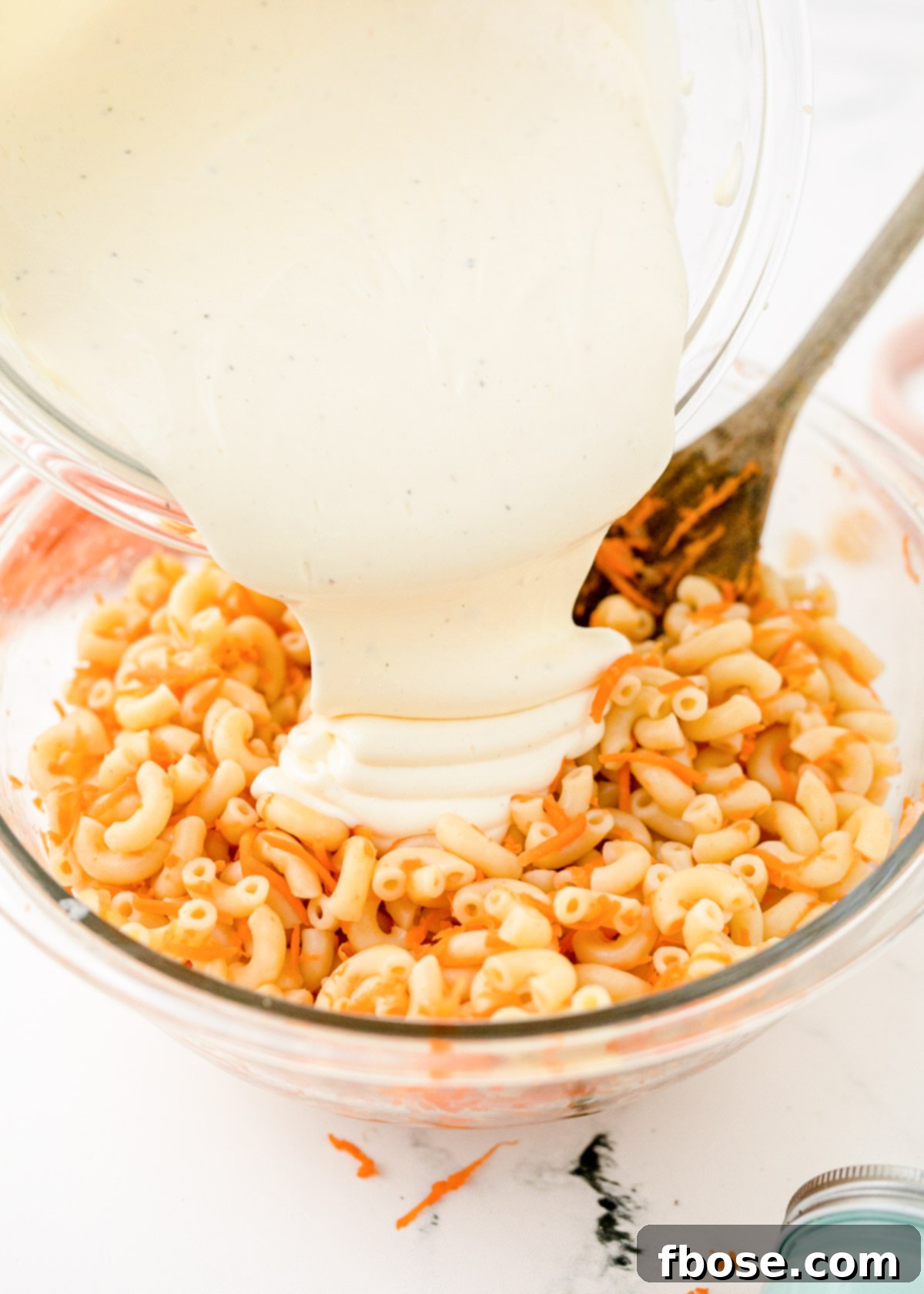 Creamy dressing being poured generously over Hawaiian Pasta Salad in a bowl.