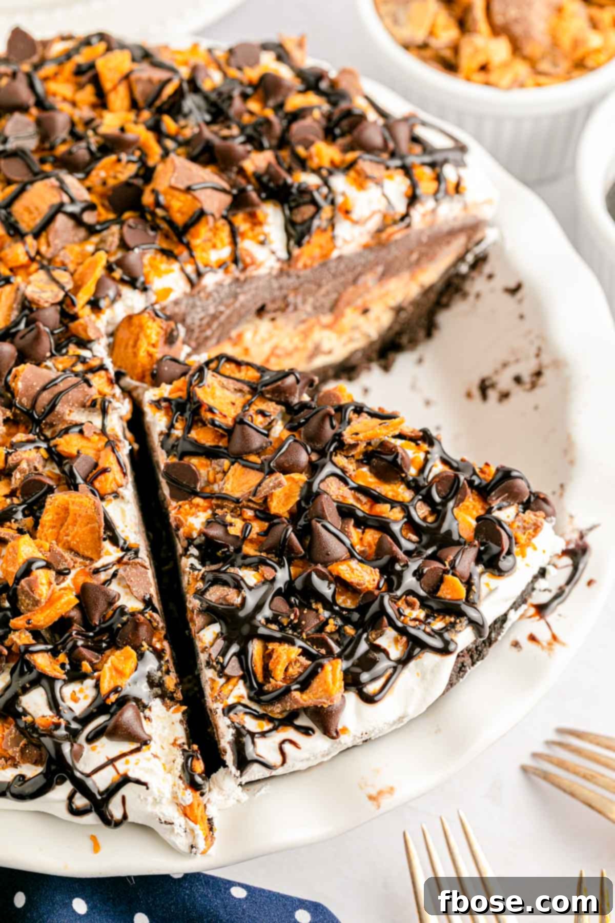 Overhead photo of a no bake butterfinger pie in a white pie dish with a slice elegantly removed, revealing the delightful layered interior and colorful candy bar toppings.