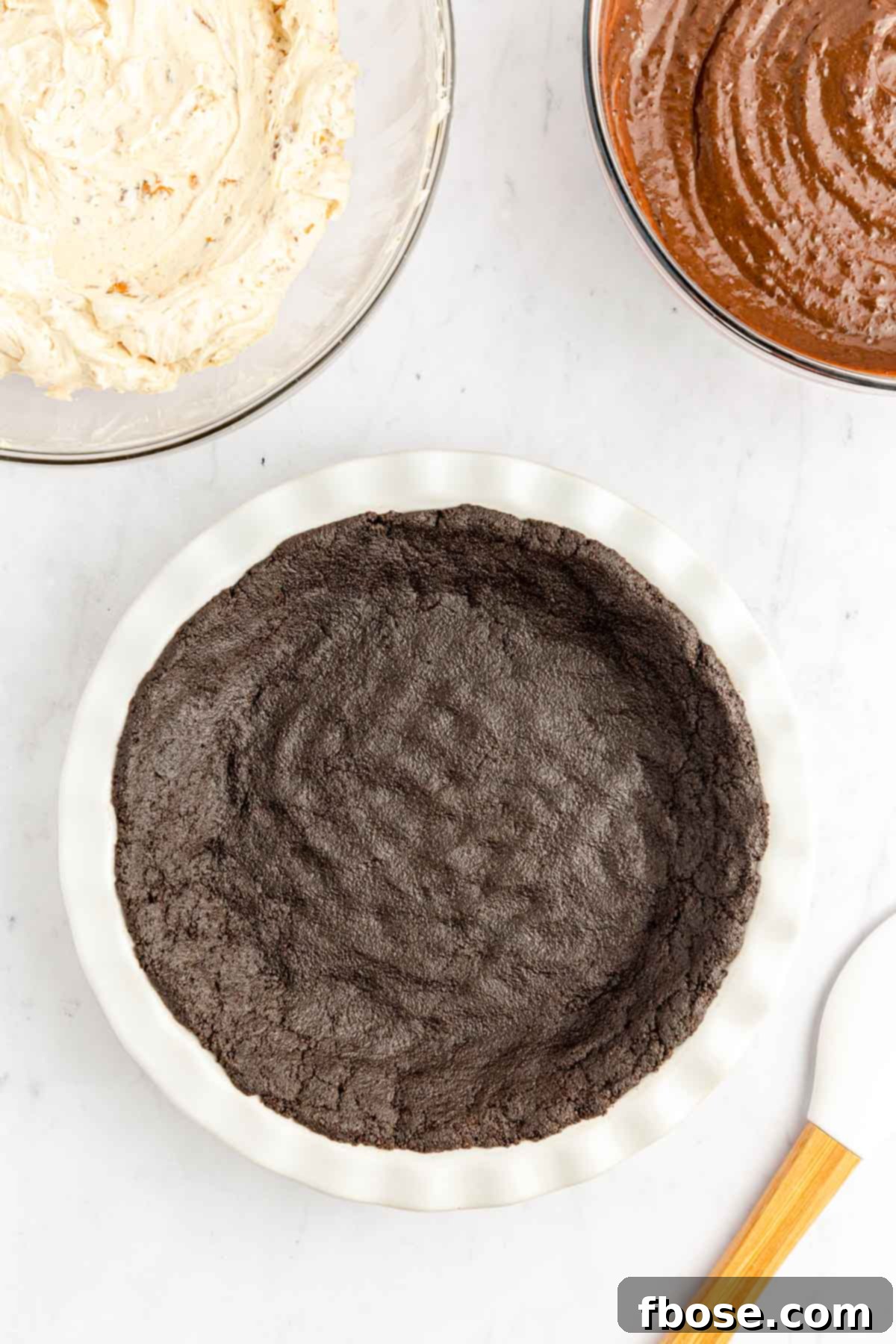 A pristine Oreo cookie crust, perfectly pressed into a white pie dish, ready for the delicious layers of filling.