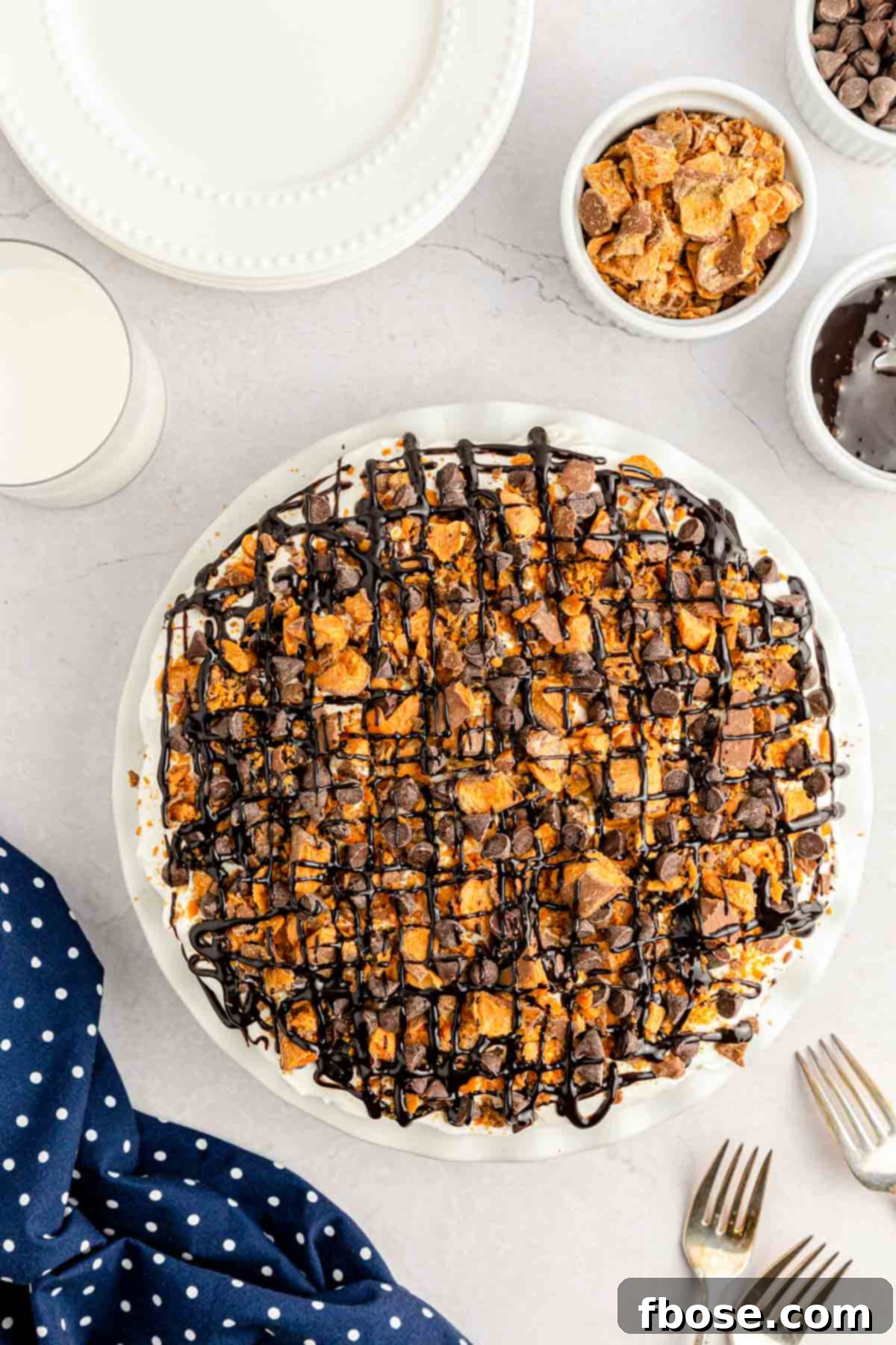 An overhead photo of the completed peanut butter pie, adorned with a final layer of Cool Whip, more Butterfinger pieces, and chocolate syrup drizzle, sitting beautifully on a table.