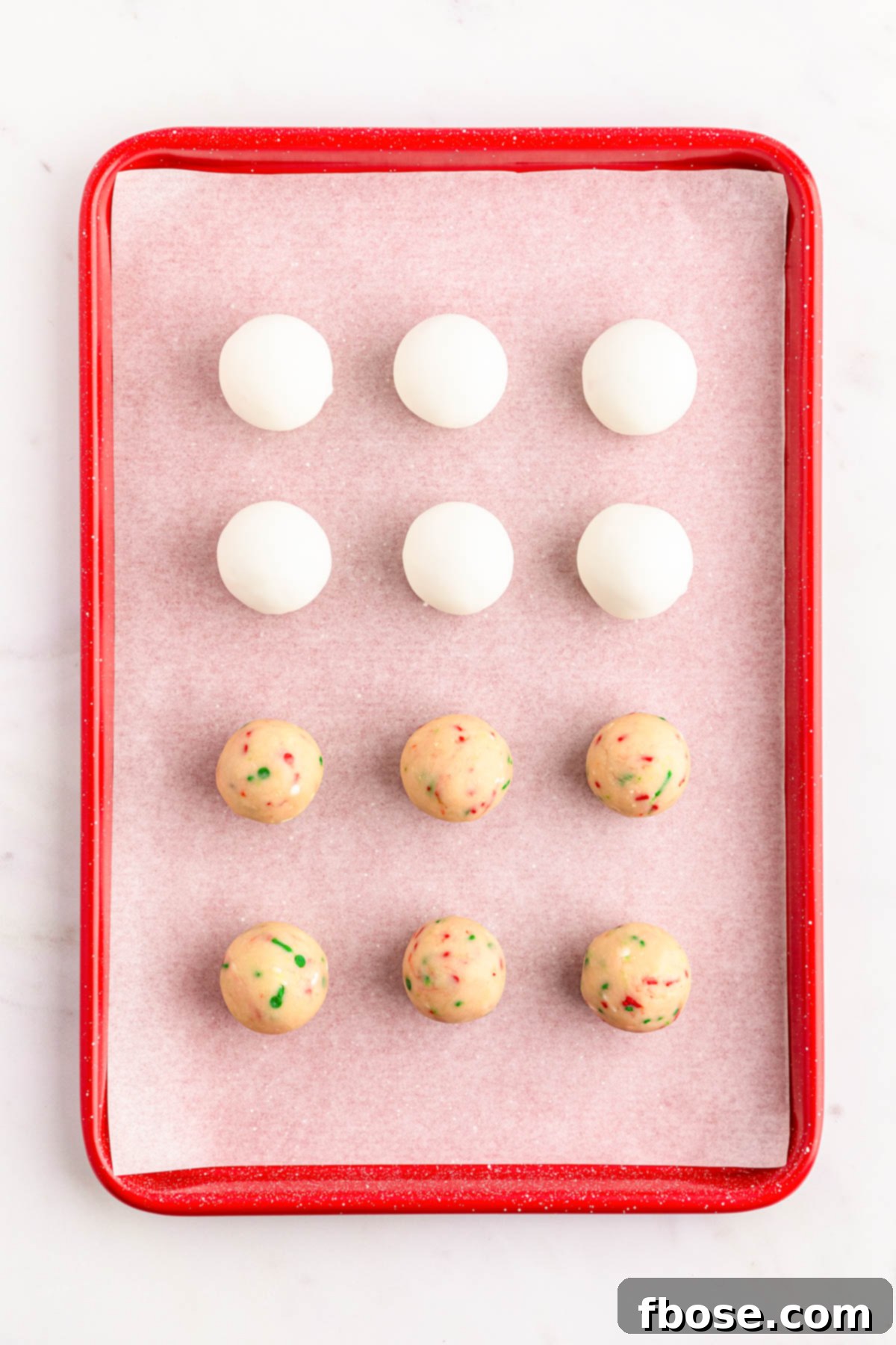 Sugar cookie balls on a parchment lined baking sheet, some dipped in white chocolate and others plain, ready for decoration.