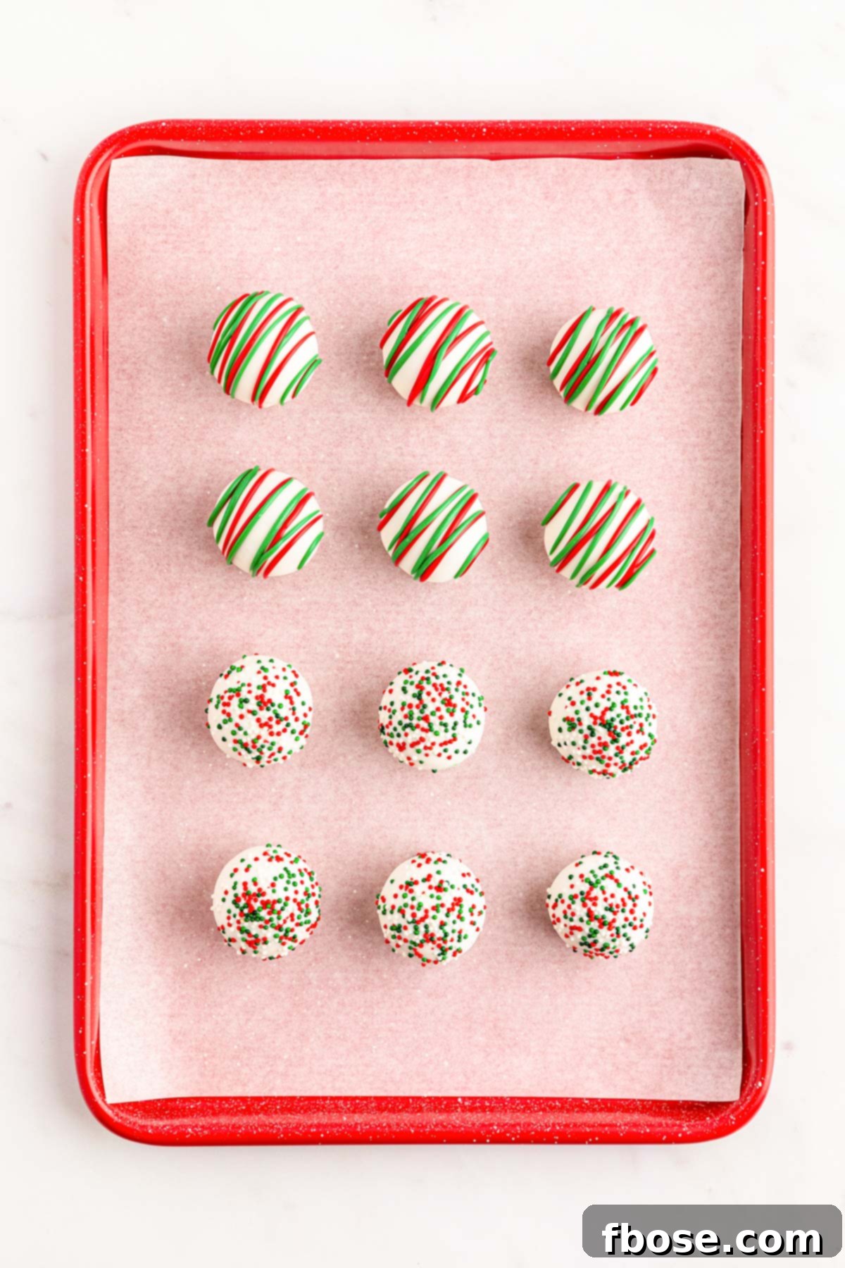 Cookie truffles decorated for Christmas with red and green drizzles and sprinkles on a baking sheet.