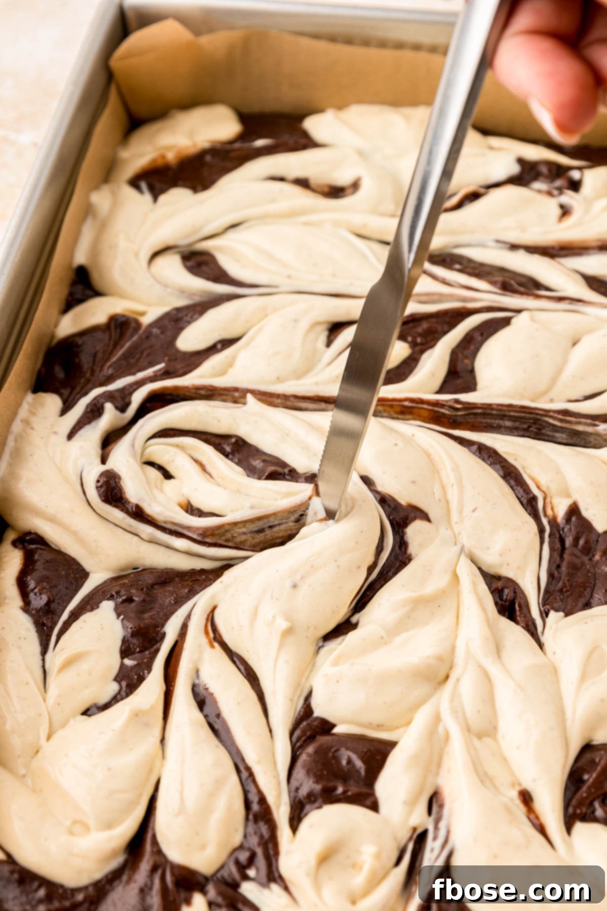 Close up of a knife swirling brownie and cheesecake batter together.