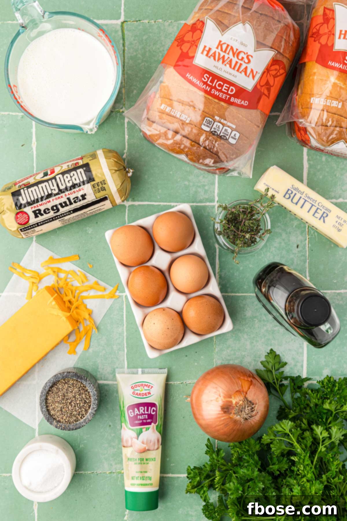 Overhead photo of all the fresh ingredients needed to make a breakfast strata, neatly arranged on a green tile surface.
