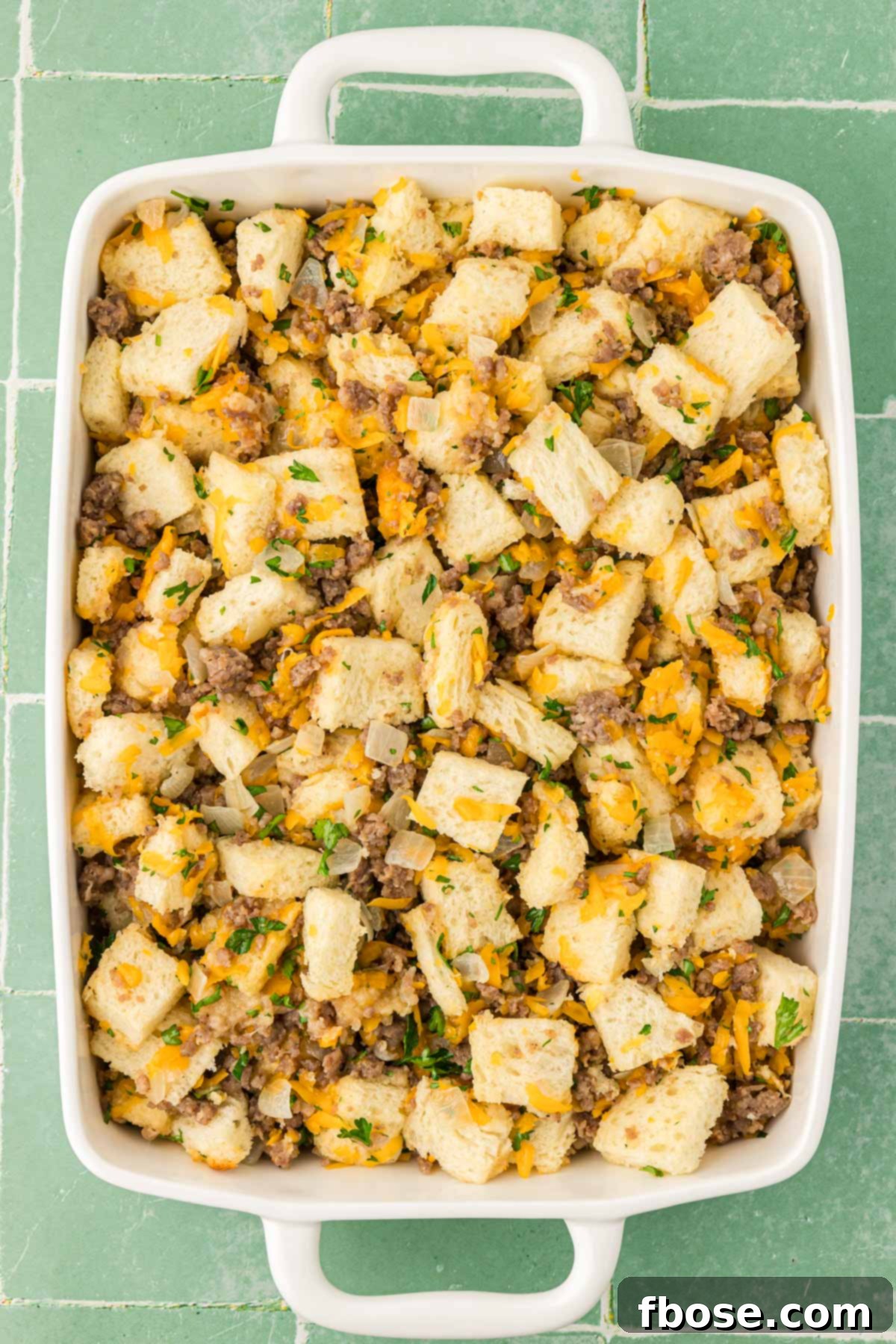 Dry ingredients for breakfast strata, including cubed bread, sausage, and cheese, spread evenly in a baking pan.