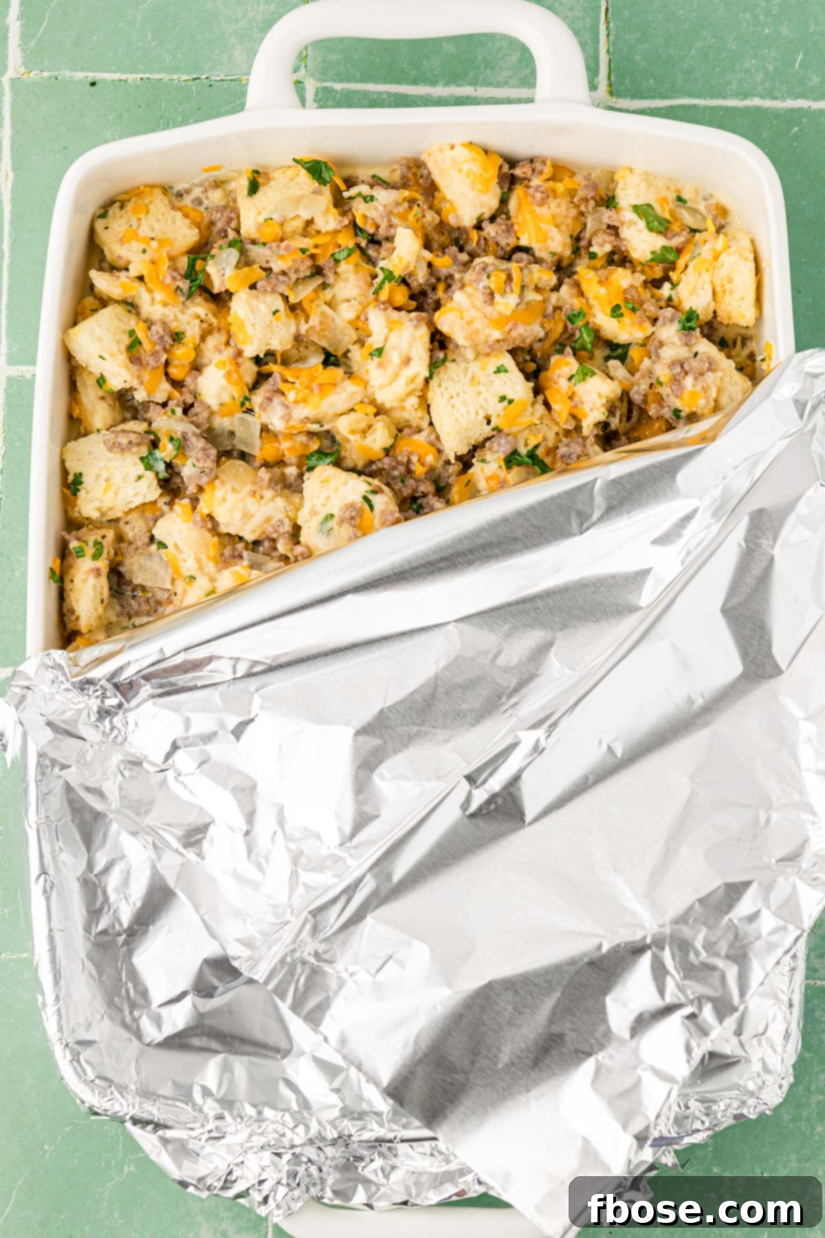 A baking pan filled with Overnight Breakfast Sausage Strata ingredients, covered with aluminum foil and ready to chill in the fridge.
