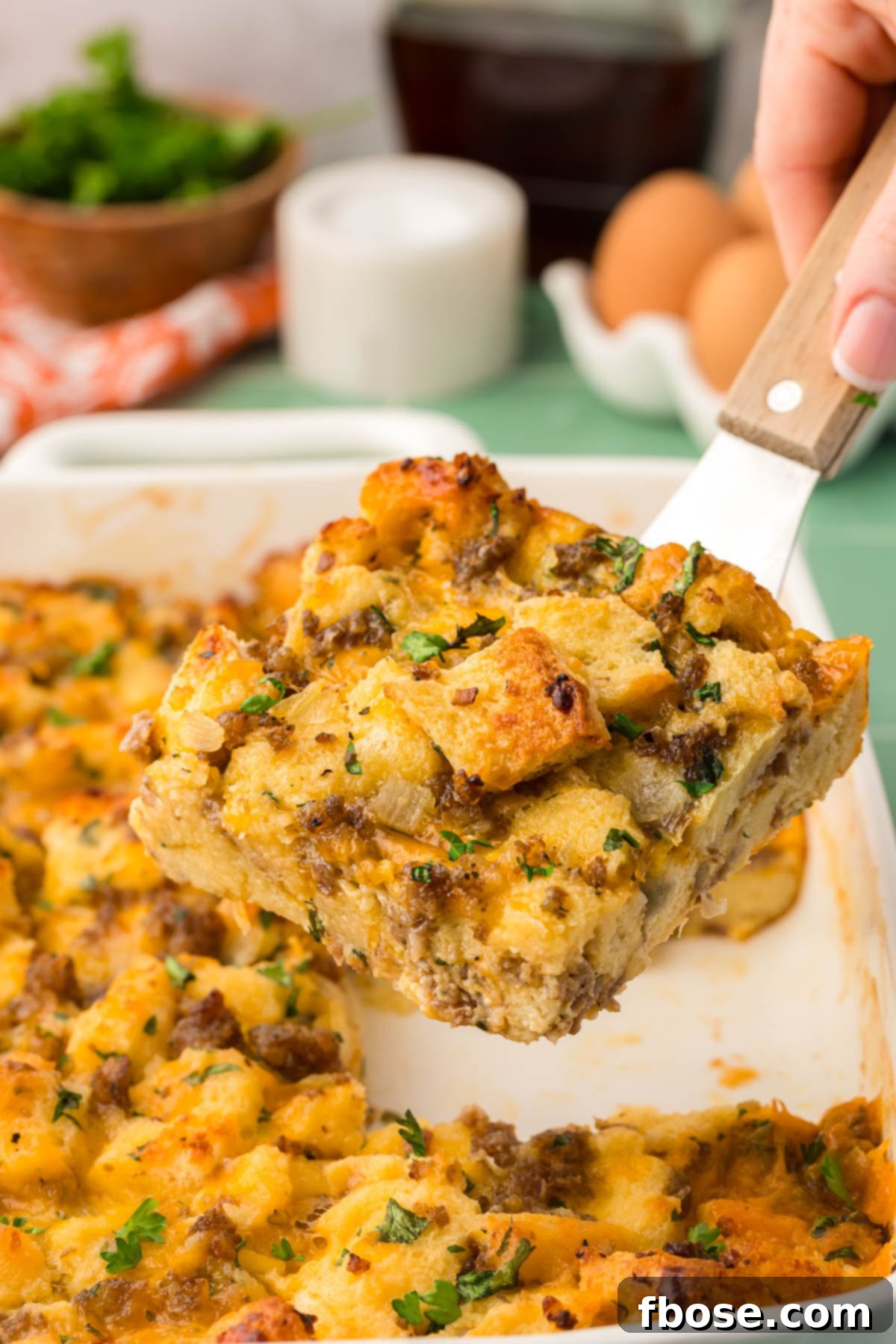 A slice of golden brown Overnight Breakfast Sausage Strata being lifted from the baking pan with a spatula, showcasing its hearty layers.