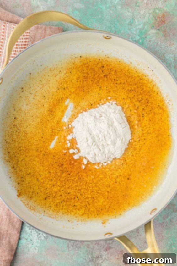 Flour being added to melted butter and spices in a skillet to begin making a roux.