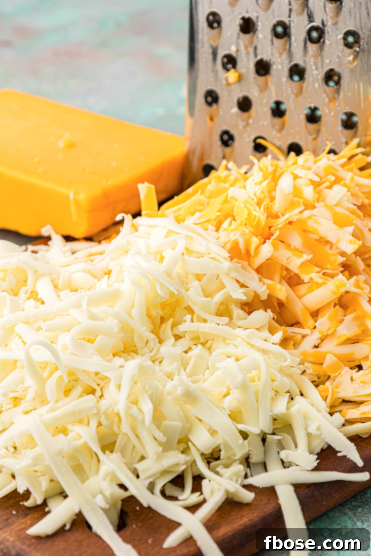 Close-up photo of fresh shredded cheese piled on a wooden cutting board.
