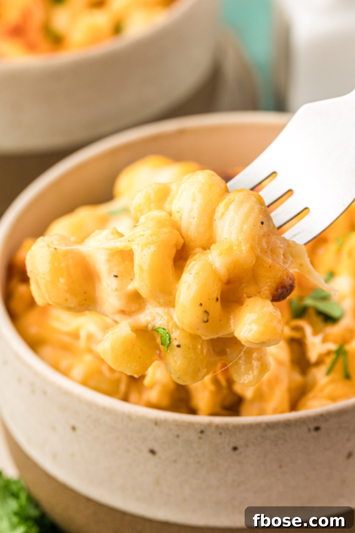 A fork scooping a perfect bite of mac and cheese out of a small white bowl.