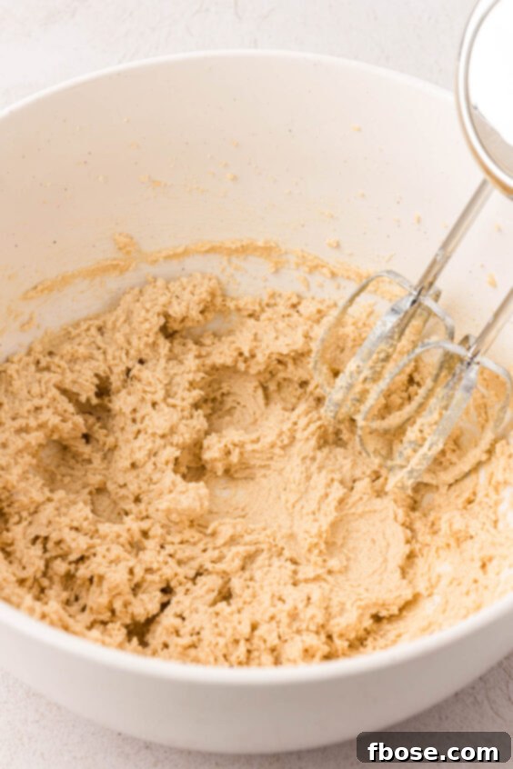 Butter and sugar being creamed by a hand mixer in a bowl.