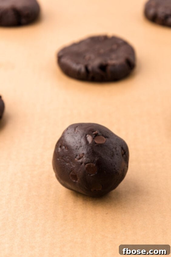 Balls of chocolate cookie dough on parchment lined baking sheet.